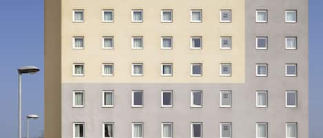 A multi-story ibis hotel with a modern facade, a central entrance, and a parking area in front.
