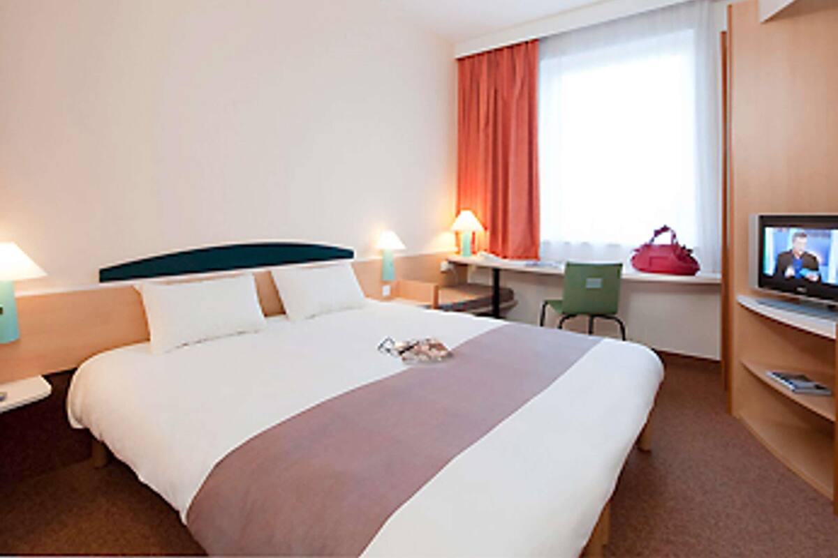 Une chambre d’hôtel équipée d’un lit, d’un bureau, d’une chaise, d’une télévision et d’une fenêtre avec des rideaux.