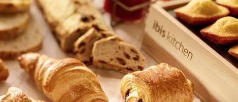 Variedad de productos horneados, incluyendo croissants y pan, dispuestos sobre una mesa con la etiqueta que dice 'Ibis Kitchen'.