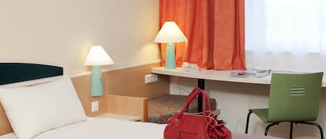Una habitación de hotel con una cama, dos lámparas de noche, un escritorio con una silla, un bolso rojo y una ventana con cortinas naranjas.