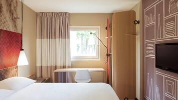 Habitación de hotel con cama, escritorio, silla, televisor y ventana con cortinas.