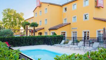 Un edificio amarillo con letreros de 'ibis', piscina y mobiliario exterior.