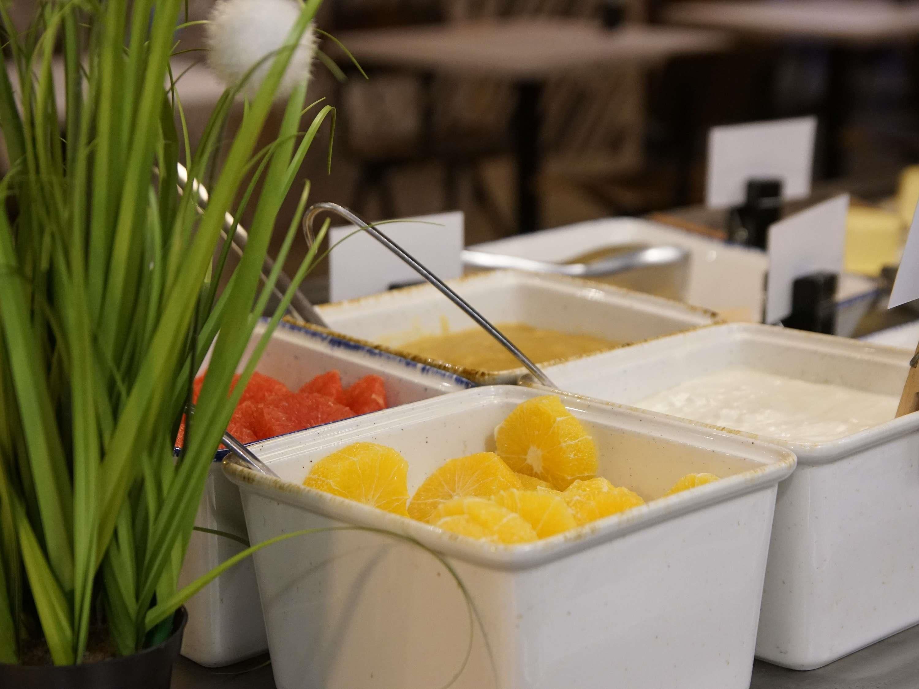 A buffet with various food items including oranges and a container with a white substance.