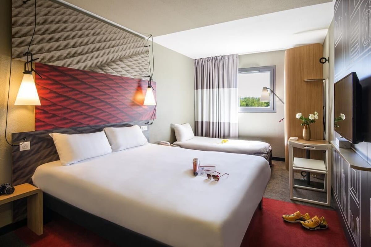 Une chambre d’hôtel avec un grand lit, deux petits lits, une télévision, un bureau et une fenêtre avec des rideaux.