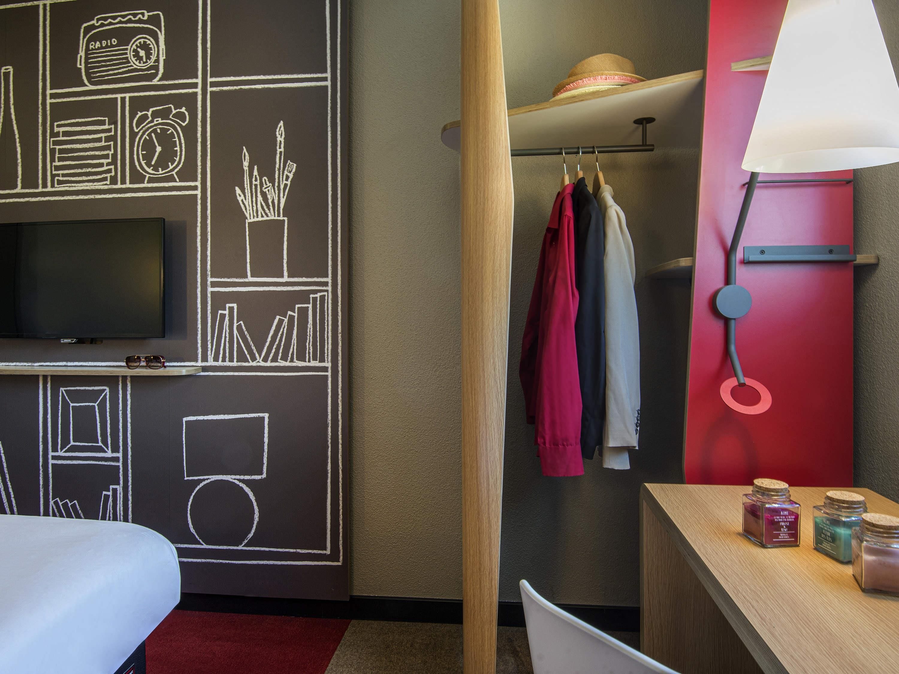 A hotel room with a television, a wall with chalkboard drawings, a wooden chair, a table with candles, and a red wall.