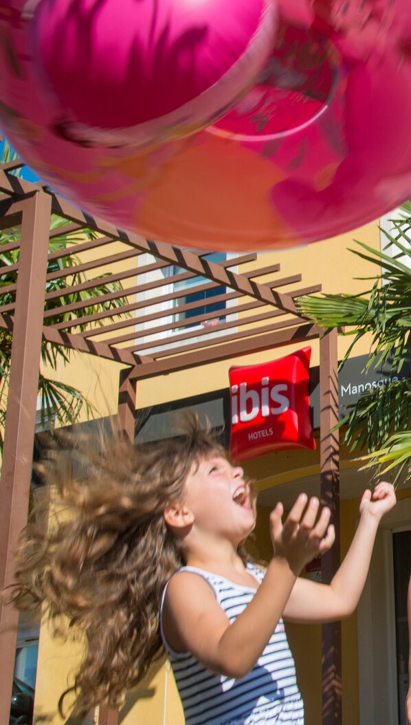 A child playing with a large pink ball under a wooden structure with a sign for ibis Hotels. - ibis Manosque Cadarache (Manosque)
