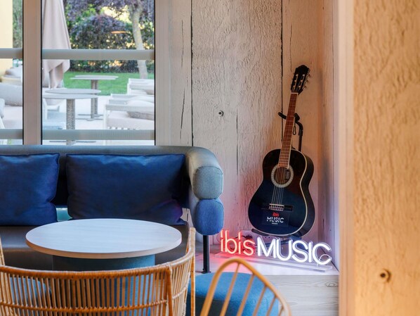 A room with a blue sofa, a round table, a wicker chair, and a guitar against a wall. - ibis Manosque Cadarache (Manosque)