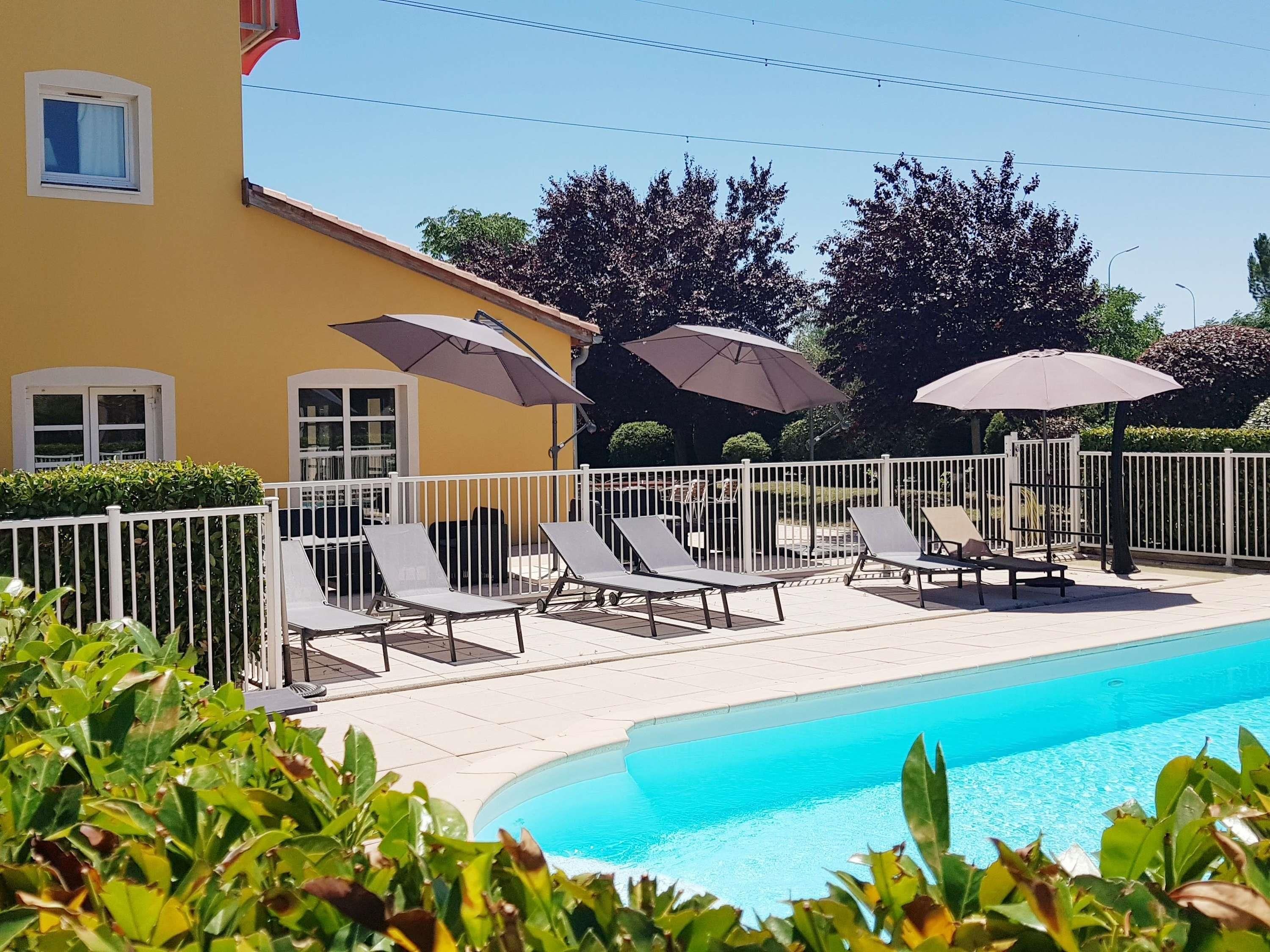 A pool area with lounge chairs and umbrellas, surrounded by a white fence and greenery.