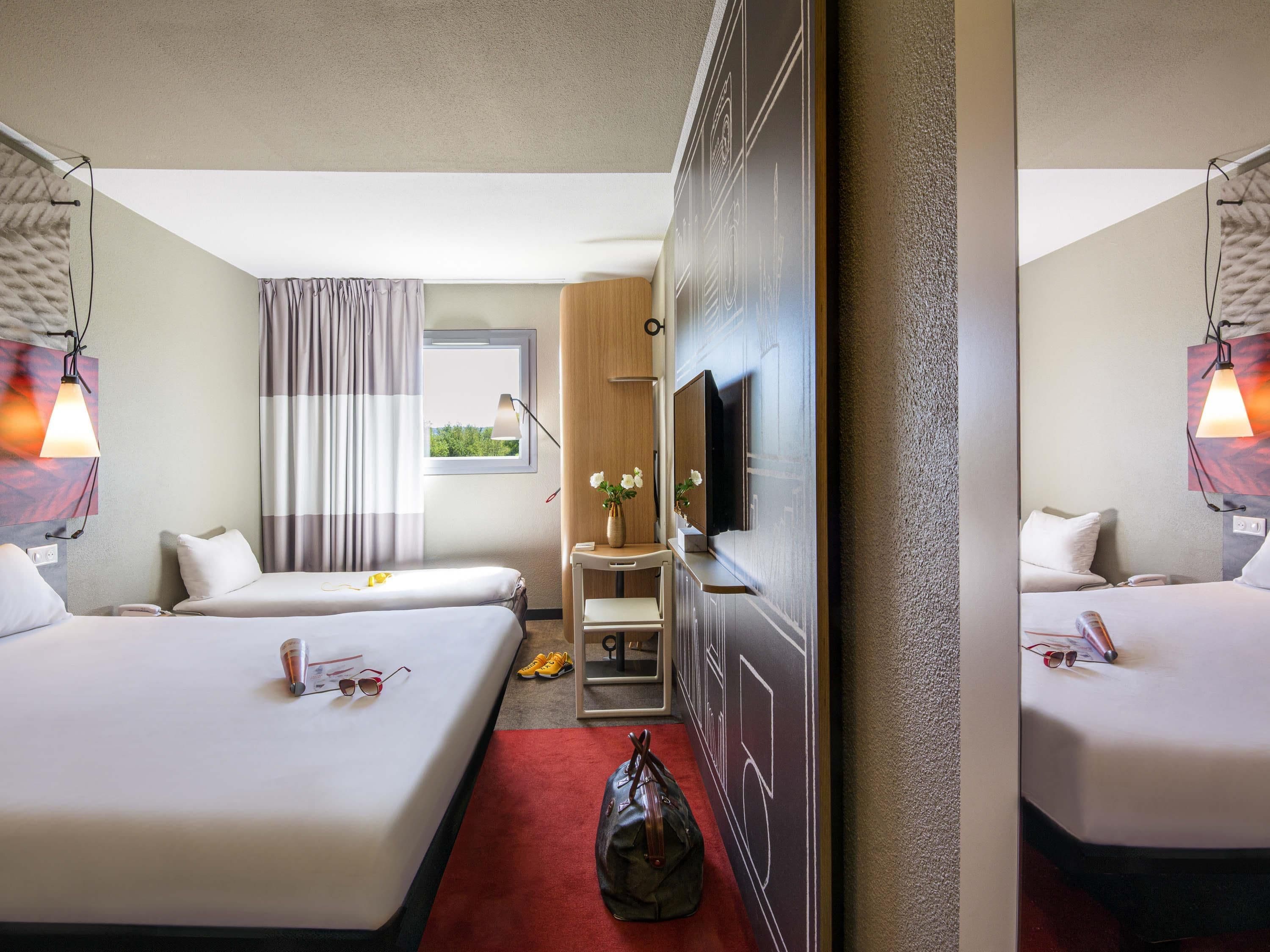 A hotel room with two beds, a TV, a desk, and a window with curtains.