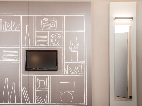Une chambre moderne avec un téléviseur à écran plat fixé sur un mur recouvert d’un tableau noir, une porte dotée d’un miroir et un luminaire placé au-dessus.