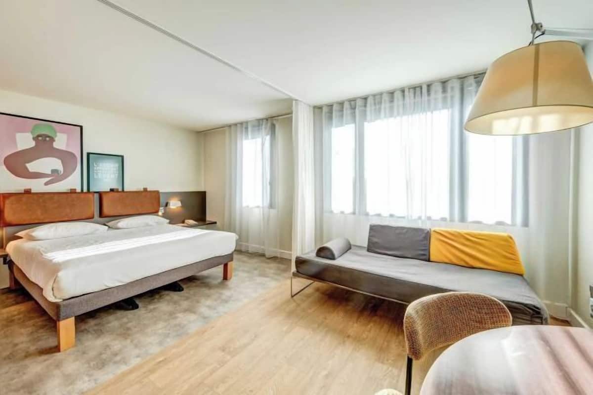 Een hotelkamer met een bed, een sofa, een tafel en een groot raam met gordijnen.