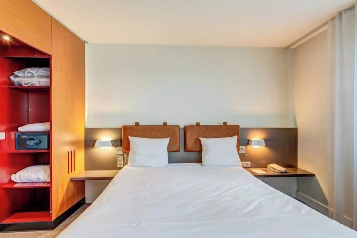 Een hotelkamer met een groot bed, twee nachtkastjes, een kledingkast en een nachtkastje met een lamp.