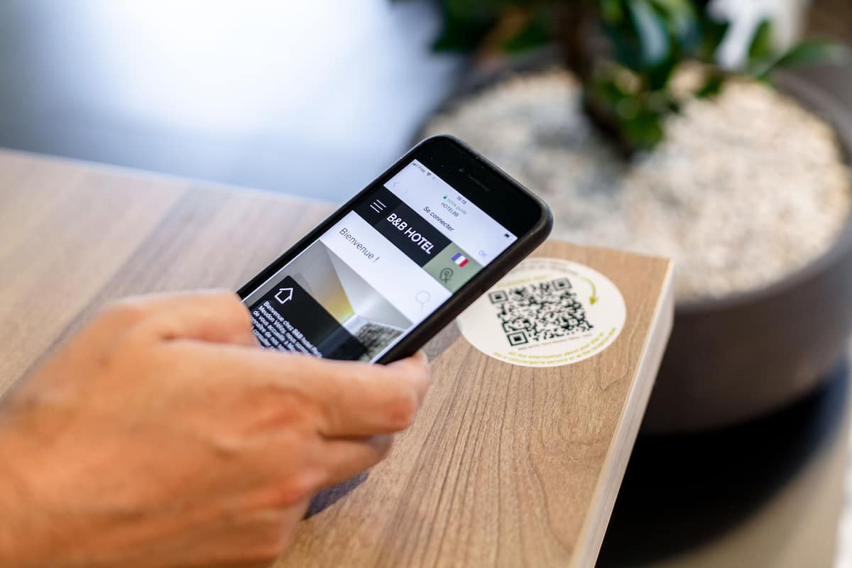 Een smartphone waarop een hotelboekings-app met een QR-code op een houten ondergrond staat.