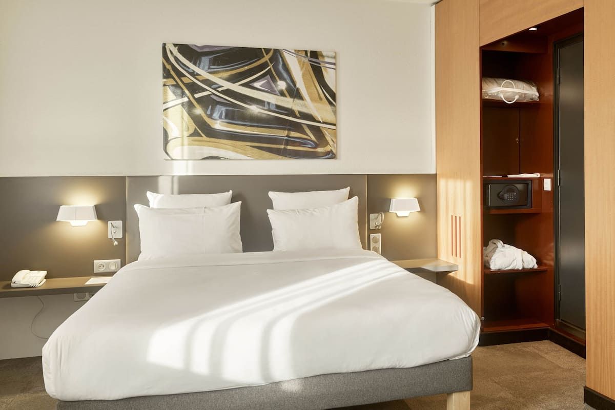 Hotelkamer met een groot bed, bedlampen, een abstract kunstwerk aan de muur, een garderobe en een klein tafeltje met een telefoon.
