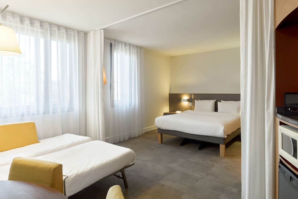 Een hotelkamer met twee bedden, een eettafel, een televisie en een magnetron.