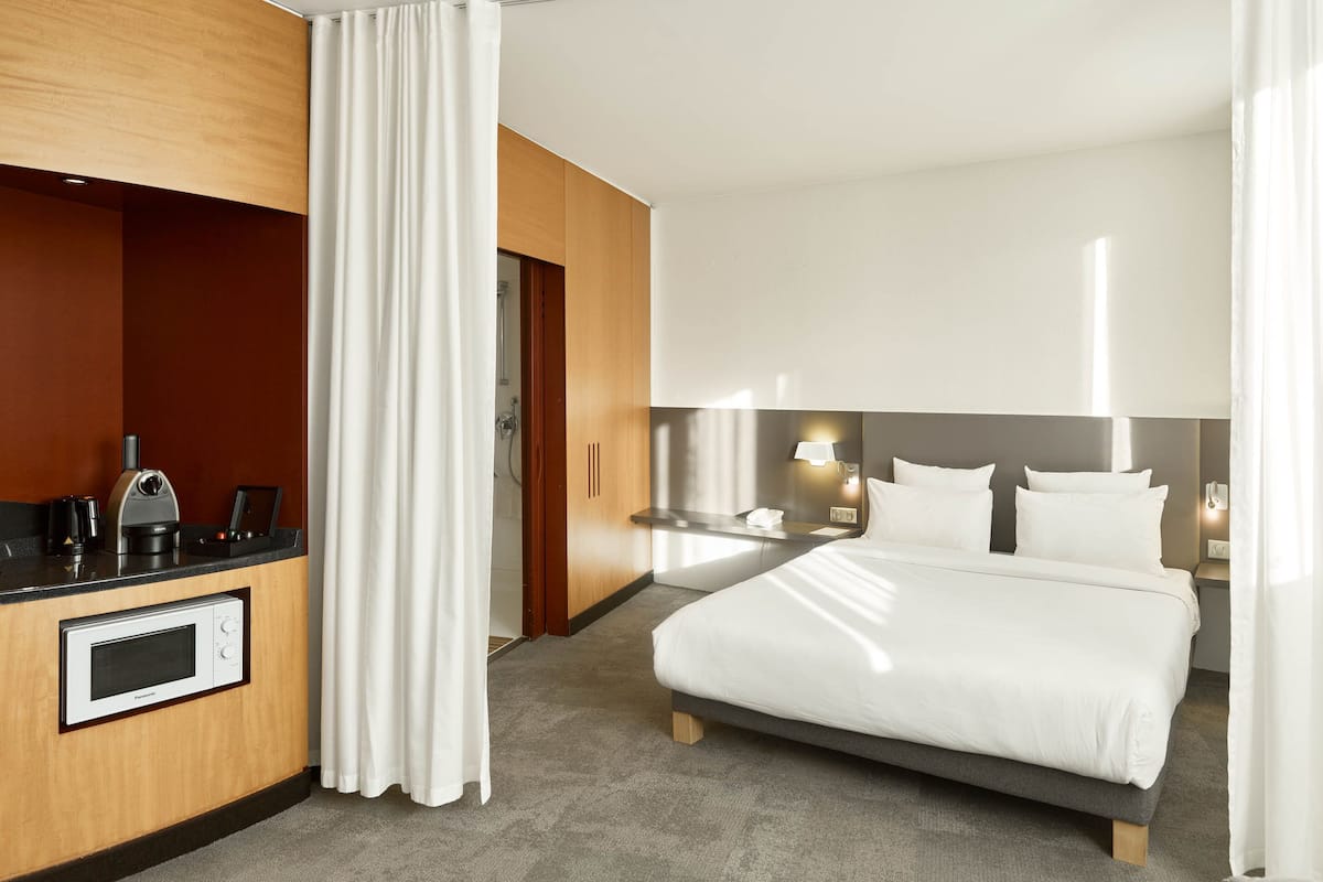 Hotelkamer met een bed, een bureau met een magnetron, een nachtkastje met een lamp en een deur naar de badkamer.