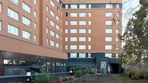 A multi-story building with a modern architectural design, featuring a mix of glass and brick facades, and a small garden area with plants and flowers.