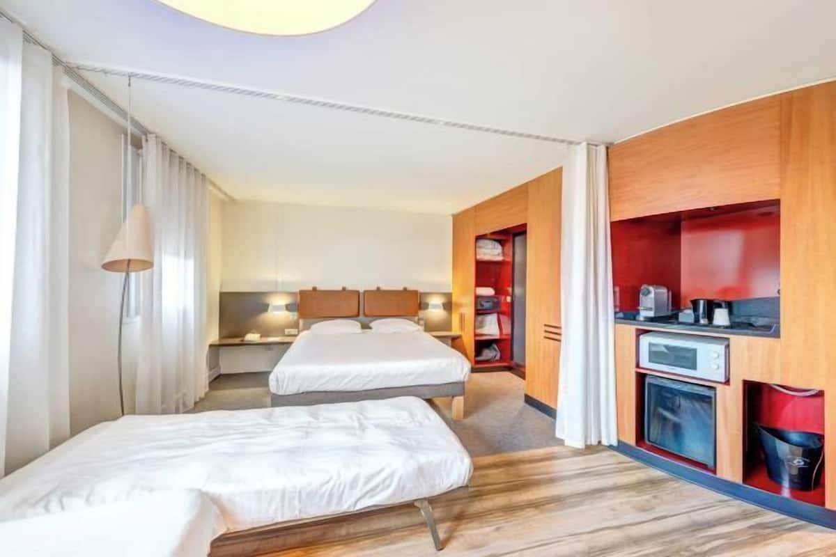 Een hotelkamer met twee bedden, een bureau, een klein keukentje en een badkamer.