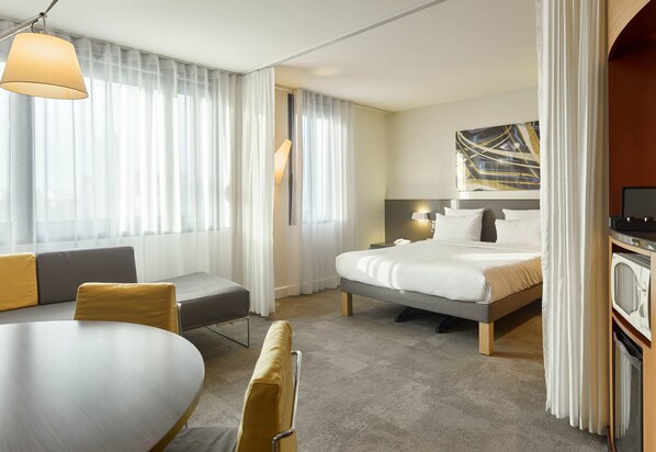 A hotel room with a bed, a sofa, a dining table, and a TV. - B&B HOME Paris Nord 18ème (Paris)