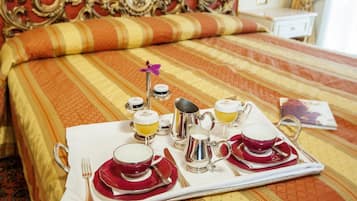 Una bandeja de desayuno ordenada con tazas, una jarra y una tetera sobre una cama con cabecera decorada y ropa de cama a rayas.