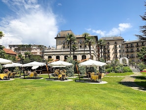 A hotel courtyard with outdoor seating and a large building in the background. - Regina Palace Hotel (Stresa)