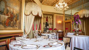 Un comedor con decoración elaborada, que incluye un cuadro grande, candelabros y mesas elegantemente dispuestas.