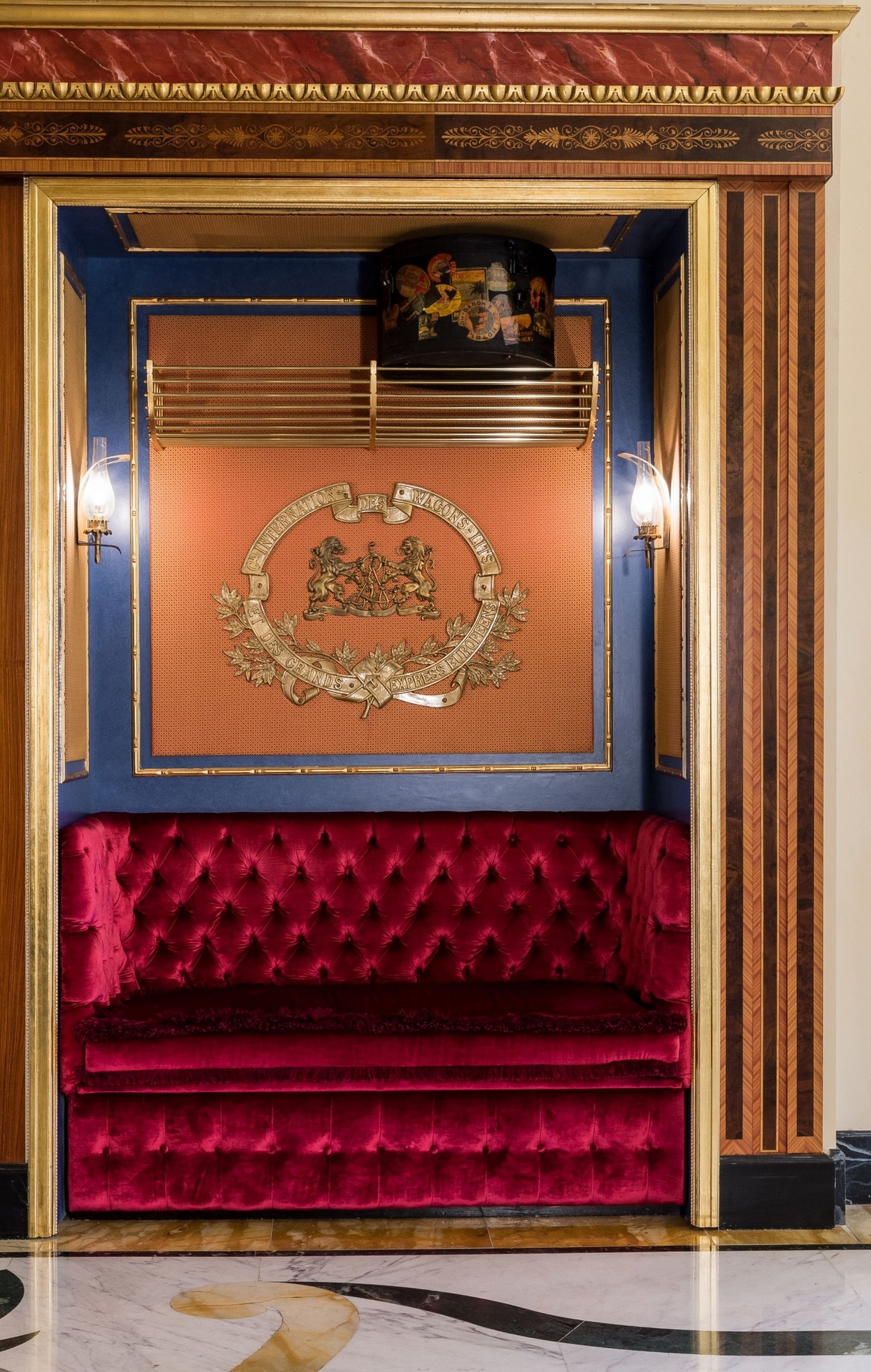 A luxurious room with a red velvet sofa, a decorative emblem on the wall, and a marble floor.