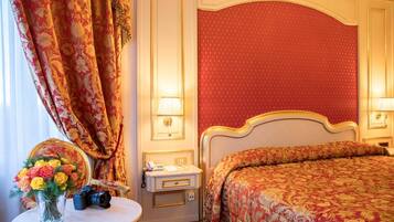 A hotel room with a bed, a bedside table with a lamp, a mirror, and a vase with flowers.