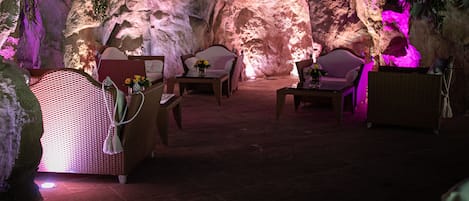 A room with a cave-like interior, furnished with wicker chairs and tables, and decorated with flowers.