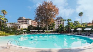 A swimming pool with lounge chairs and umbrellas, surrounded by buildings and trees. - Regina Palace Hotel (Stresa)