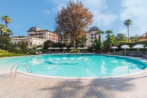 A swimming pool with lounge chairs and umbrellas, surrounded by buildings and trees. - Regina Palace Hotel (Stresa)