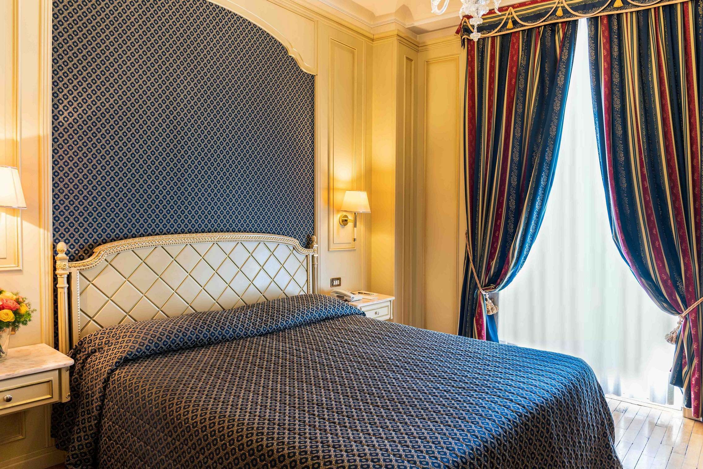 A hotel room with a bed, a nightstand, a lamp, and a window with curtains.