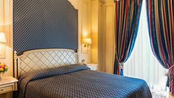 A hotel room with a bed, a nightstand, a lamp, and a window with curtains.