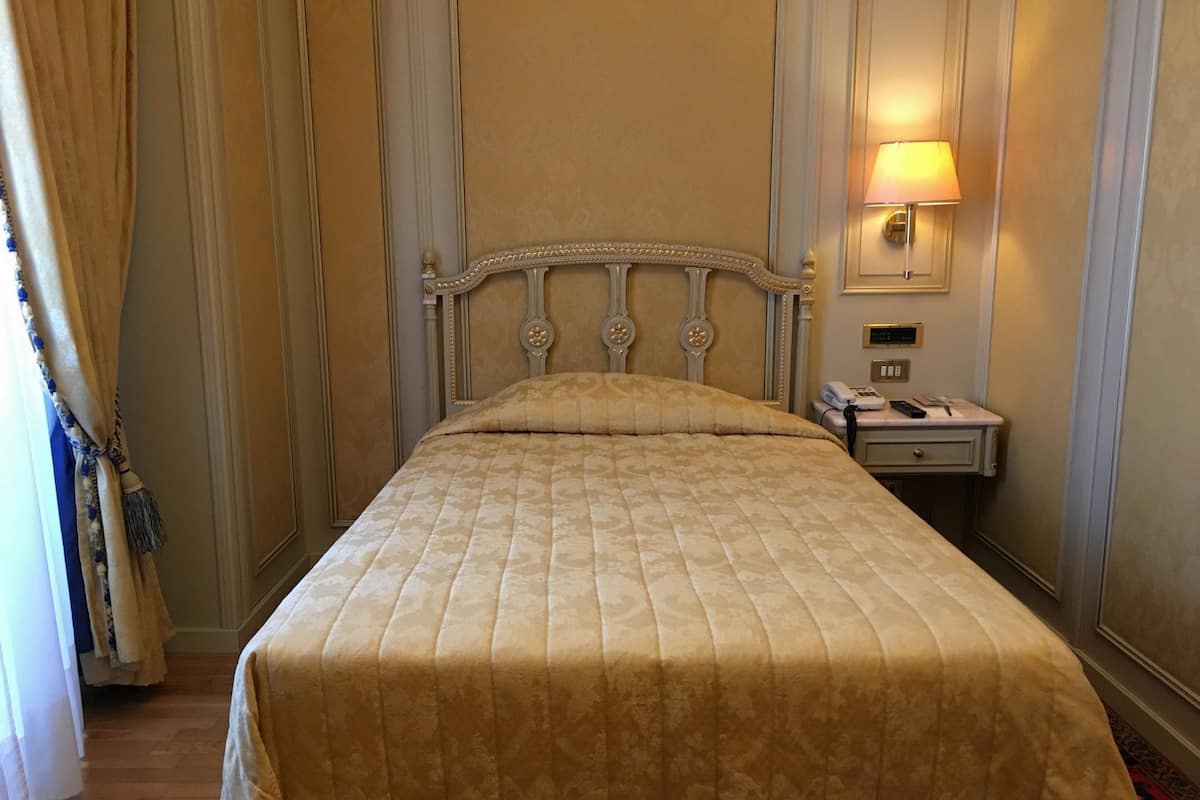 Une chambre d’hôtel avec un grand lit, une table de chevet avec une lampe et une porte avec des rideaux.