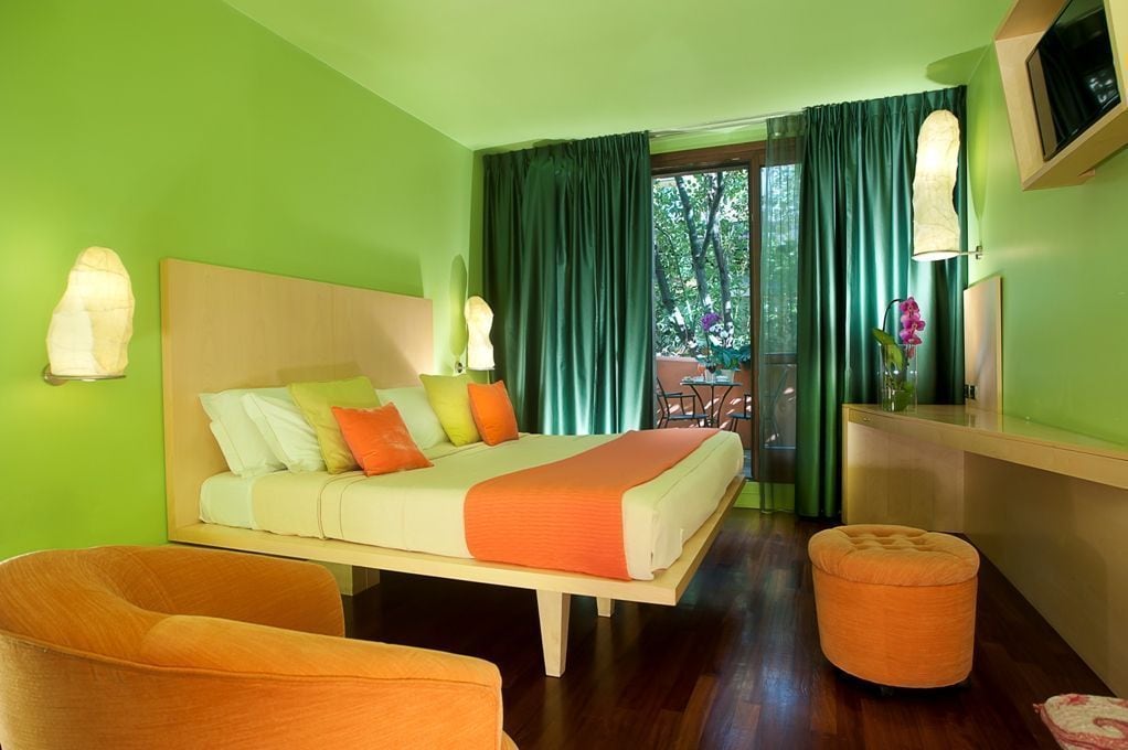 Quarto de hotel com uma cama, uma cadeira, uma mesa pequena e vista para o exterior.