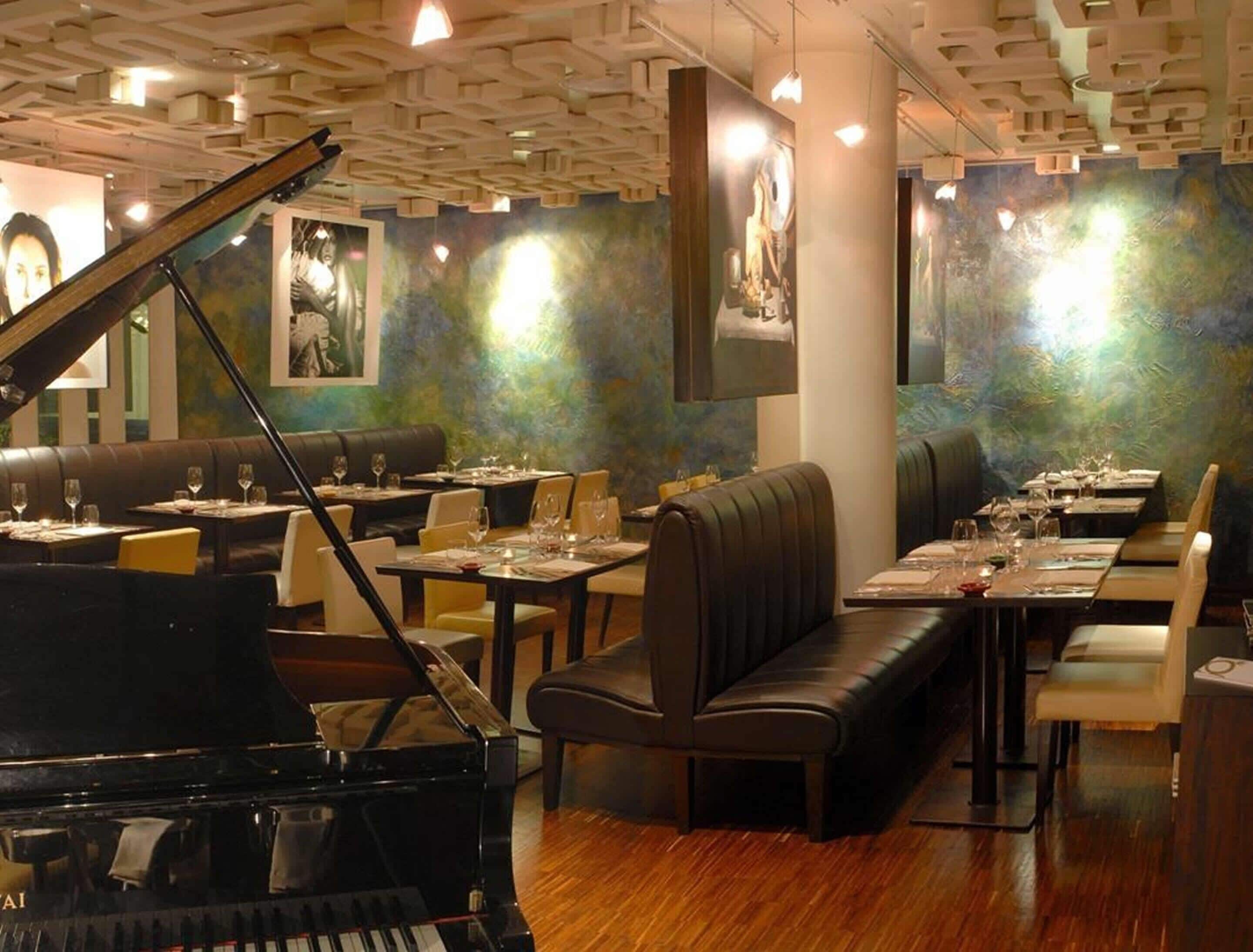 A restaurant with a grand piano, booths, and tables set for dining.