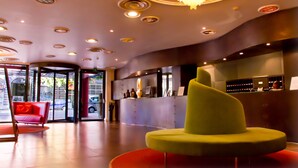 Een moderne lobby met een receptiebalie, een bijzondere groene stoel en een kroonluchter.