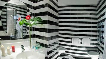 Ein modernes Badezimmer mit schwarz-weißen Streifenfliesen, einem großen Spiegel und einem Waschbecken mit Pflegeprodukten.