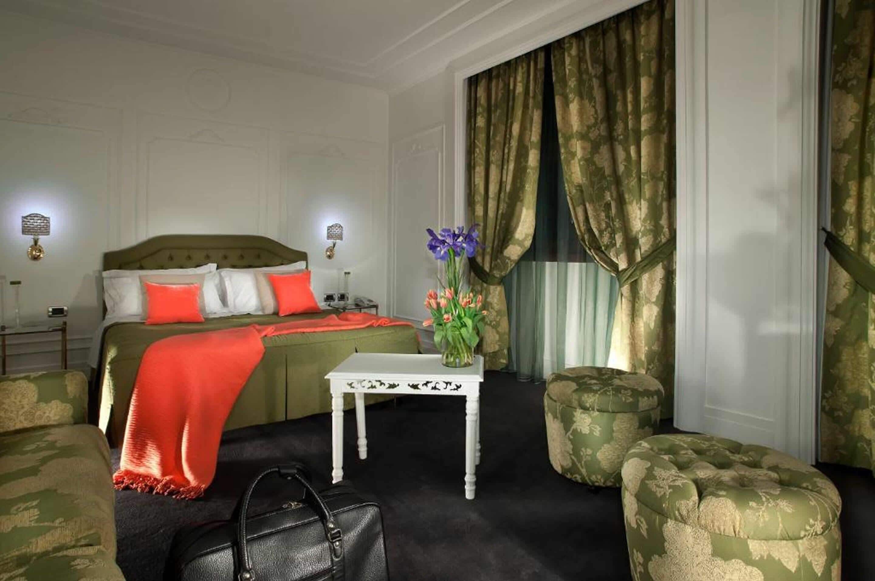 Habitació d'hotel amb un llit, una taula petita, una cadira, un sofà i una finestra amb cortines.