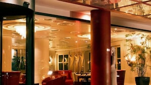 Een hotellobby met een modern design, met een groot glazen dak, rode zitplaatsen en een centrale kolom.