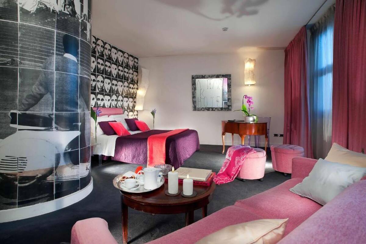 Habitación de hotel con cama, sofá, una mesita con una bandeja de comida, una silla y un espejo en la pared.