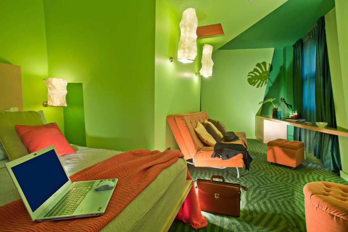 Habitación de hotel con una cama, un escritorio con una computadora portátil, una silla, una mesita y una planta.