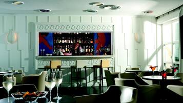 Zona de bar con un barman, una estantería repleta de licores y asientos para los clientes.