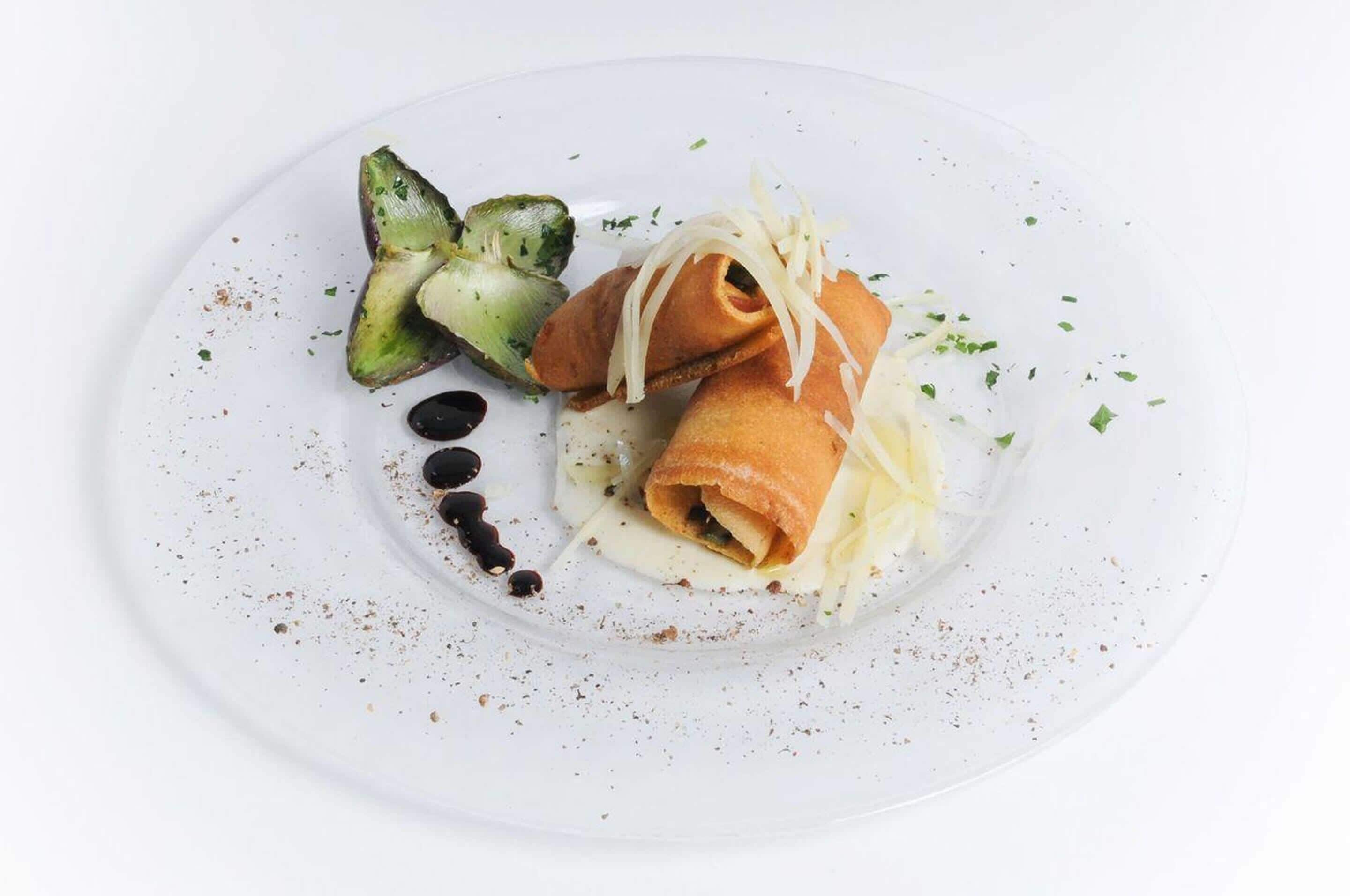 A white plate with a rolled pastry, a piece of broccoli, and a drizzle of sauce.