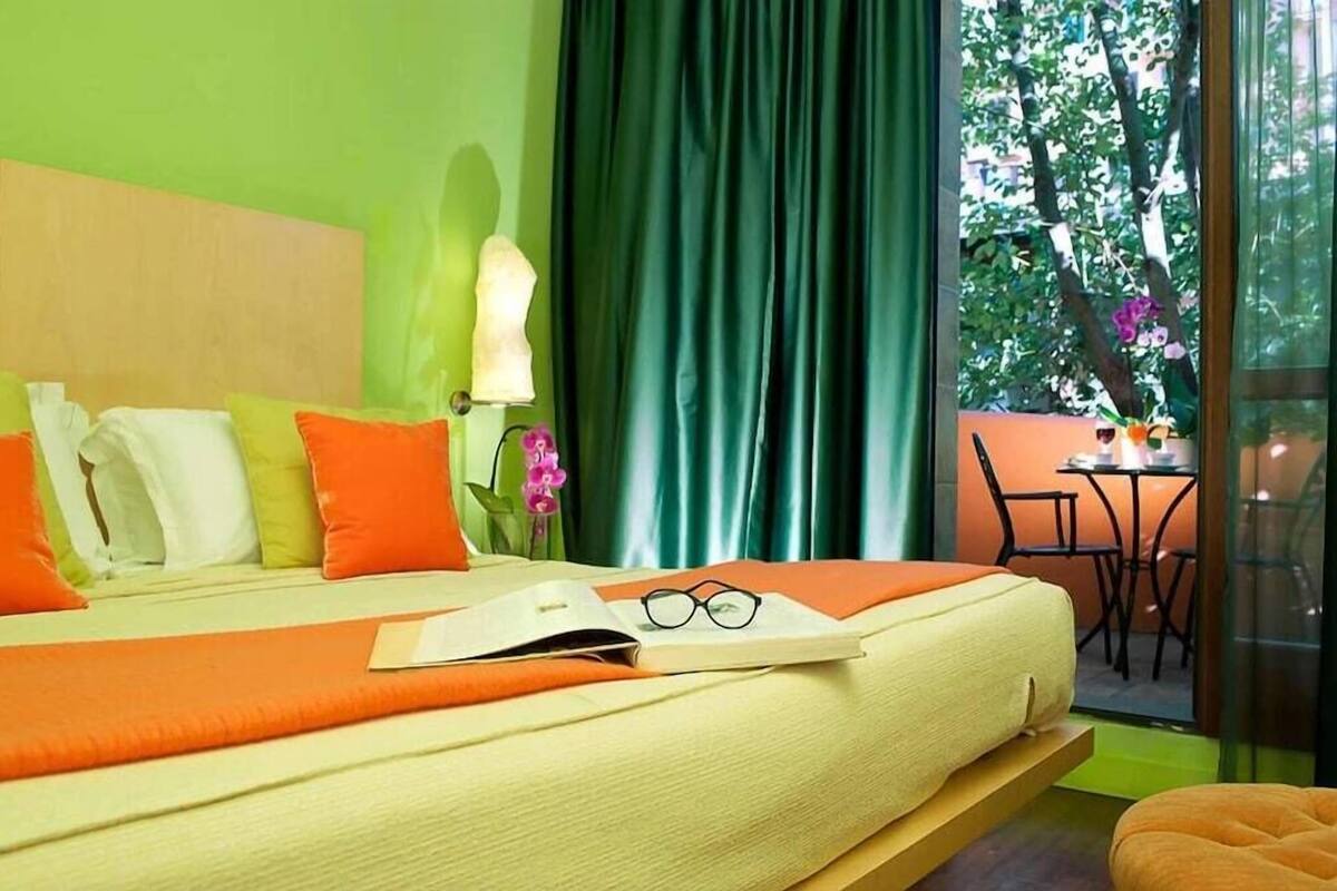 Una cama con almohadas, una mesita de noche con una lámpara y vistas a un espacio exterior con una mesa y sillas.