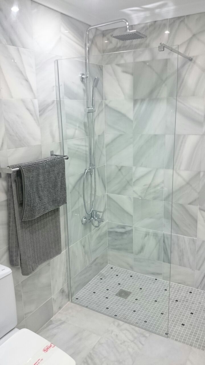 Eine gläserne Duschkabine mit Handbrause und am Wand montiertem Wasserhahn.