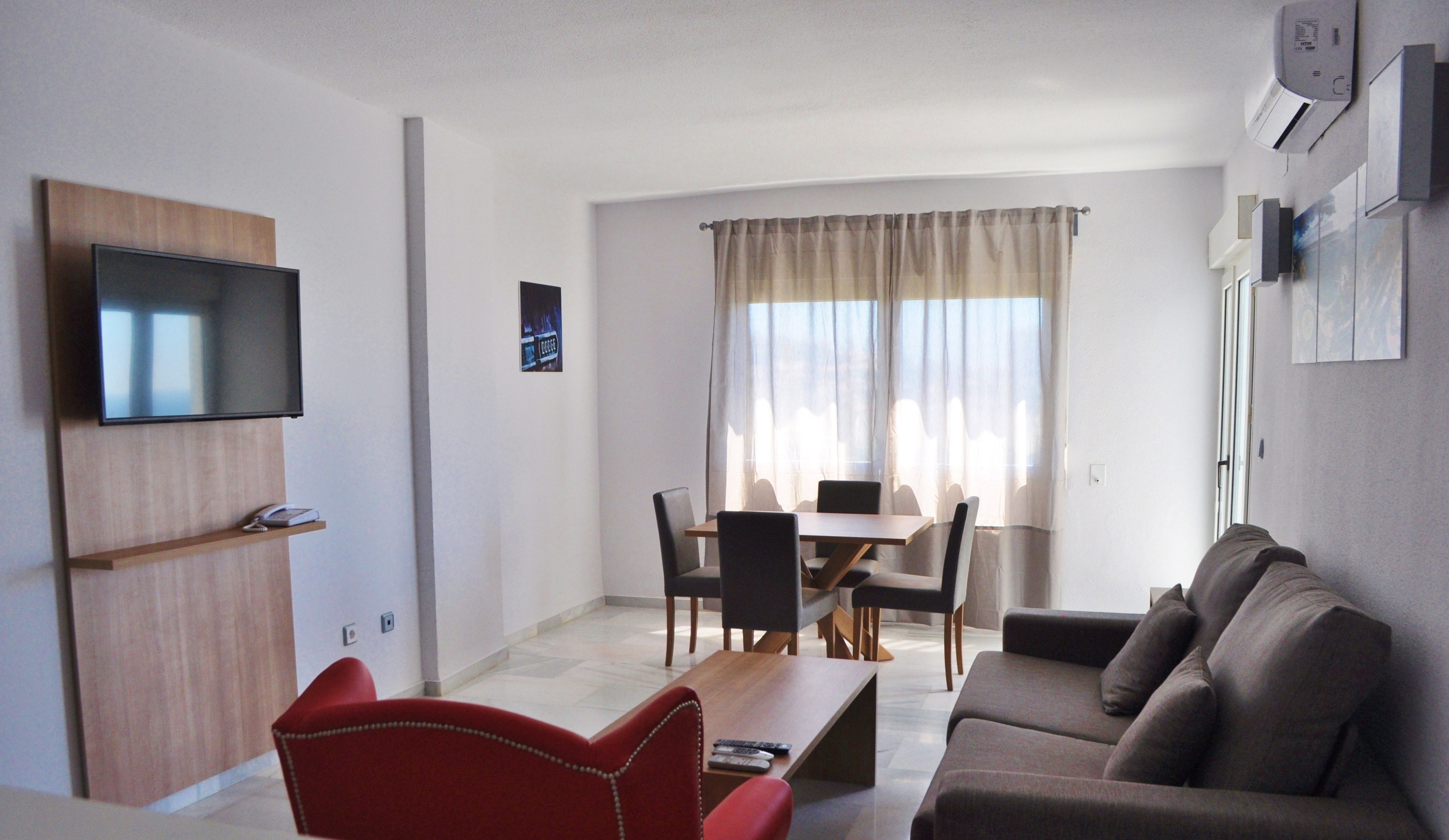 A modern living room with a flat-screen TV, a dining area with a table and chairs, and a sofa.