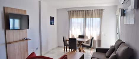 Una sala moderna con un televisor de pantalla plana, un comedor con mesa y sillas, y un sofá.