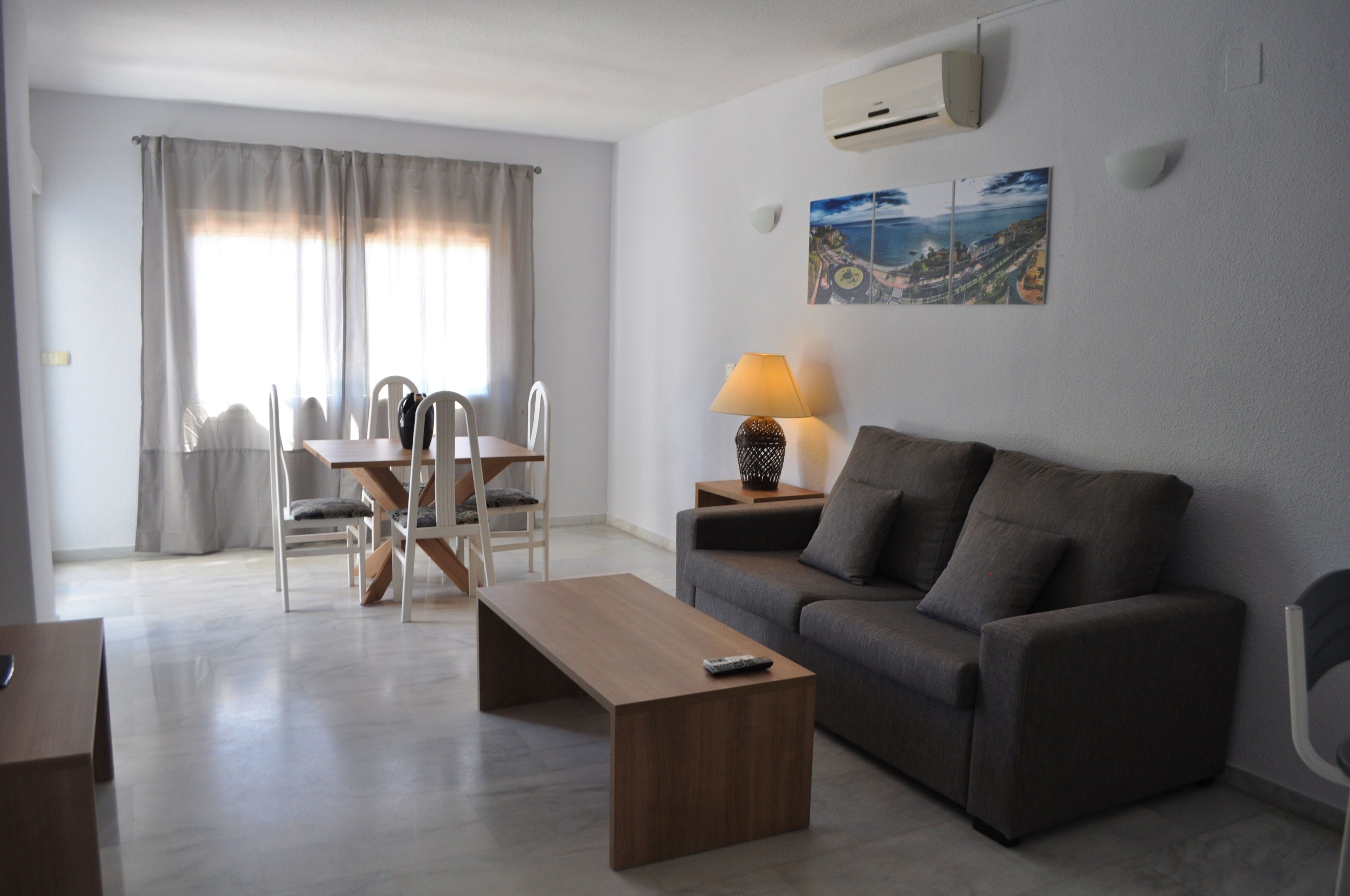 A modern living room with a sofa, a coffee table, a dining table with chairs, and a painting on the wall.