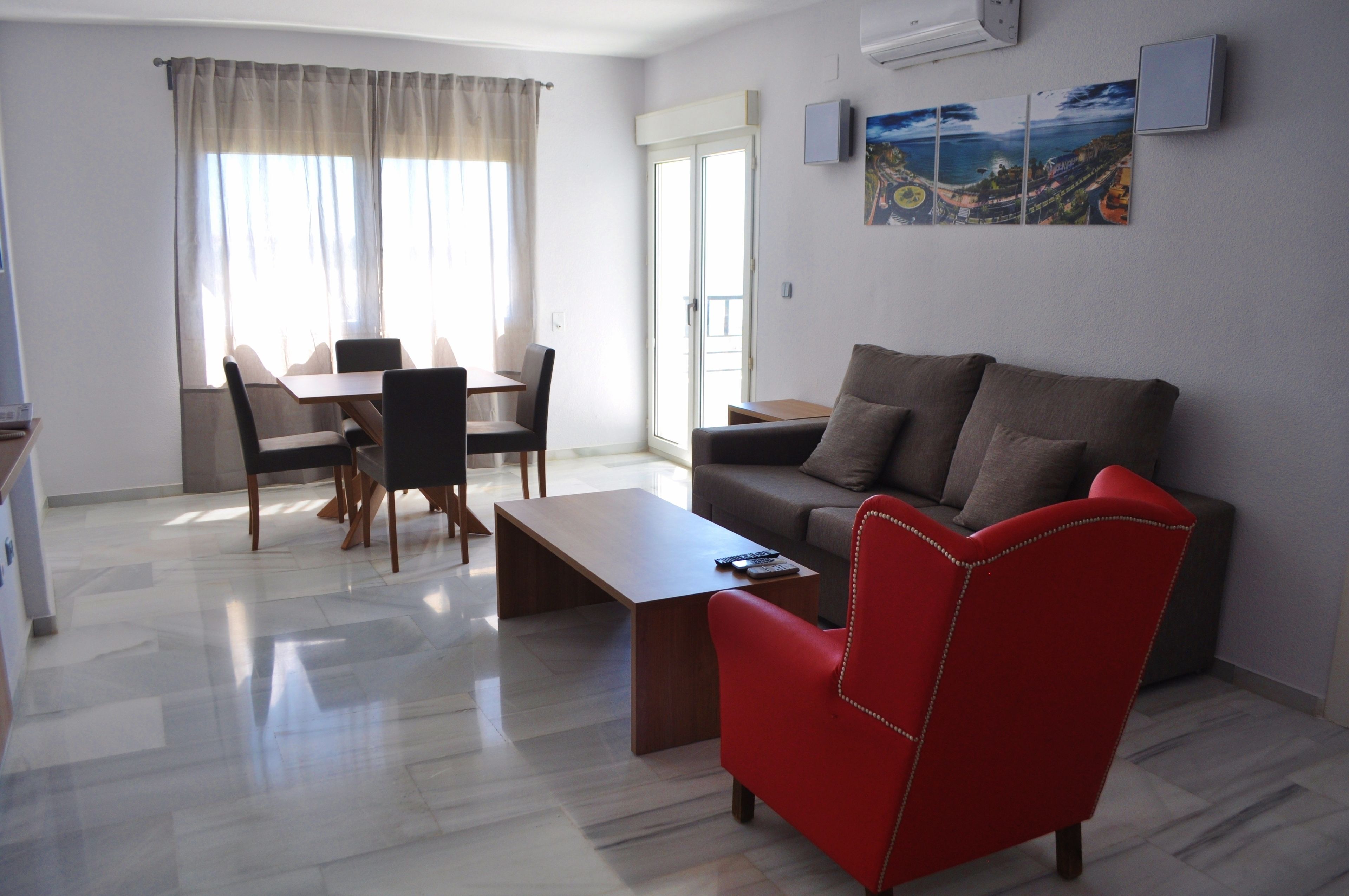 A modern living room with a sofa, a red chair, a coffee table, and a dining area with chairs and a table.